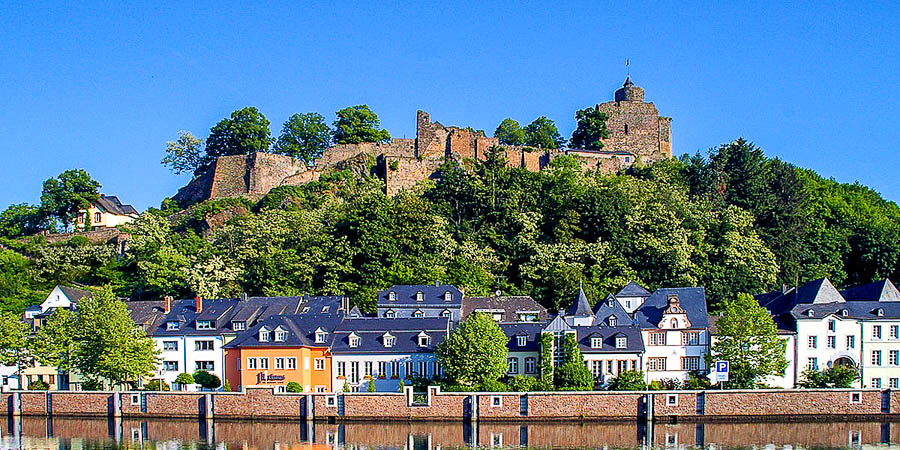 Eine Burg mit Häusern und einem Fluss davor in Saarburg